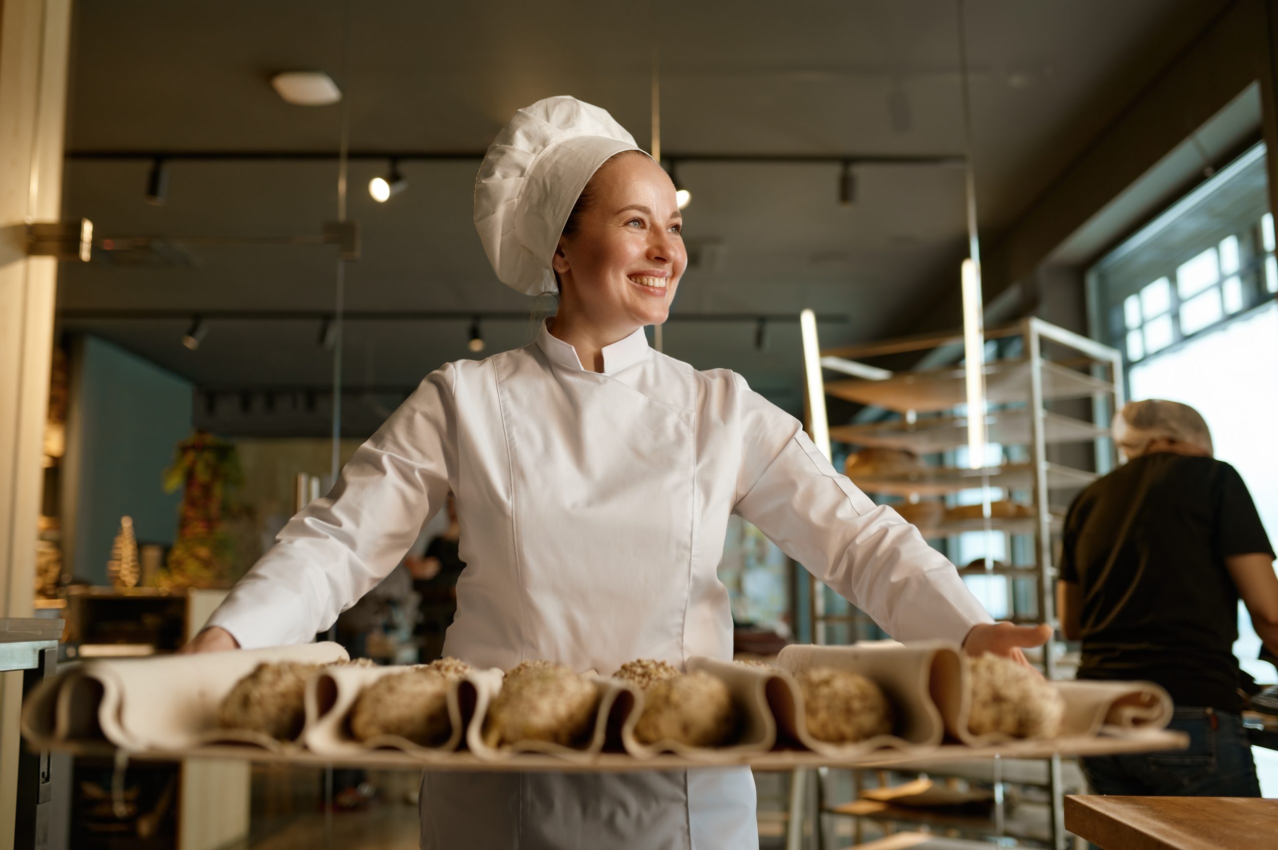 Smiling baker preparing sweet buns pastries with sesame seeds