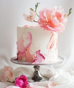 white and pink cake on a metal stand with pink flowers