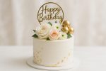 Beautiful White Birthday Cake Decorated With Flowers and a Golden Happy Birthday Topper