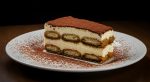 A delectable slice of tiramisu on a white plate, sprinkled with cocoa powder