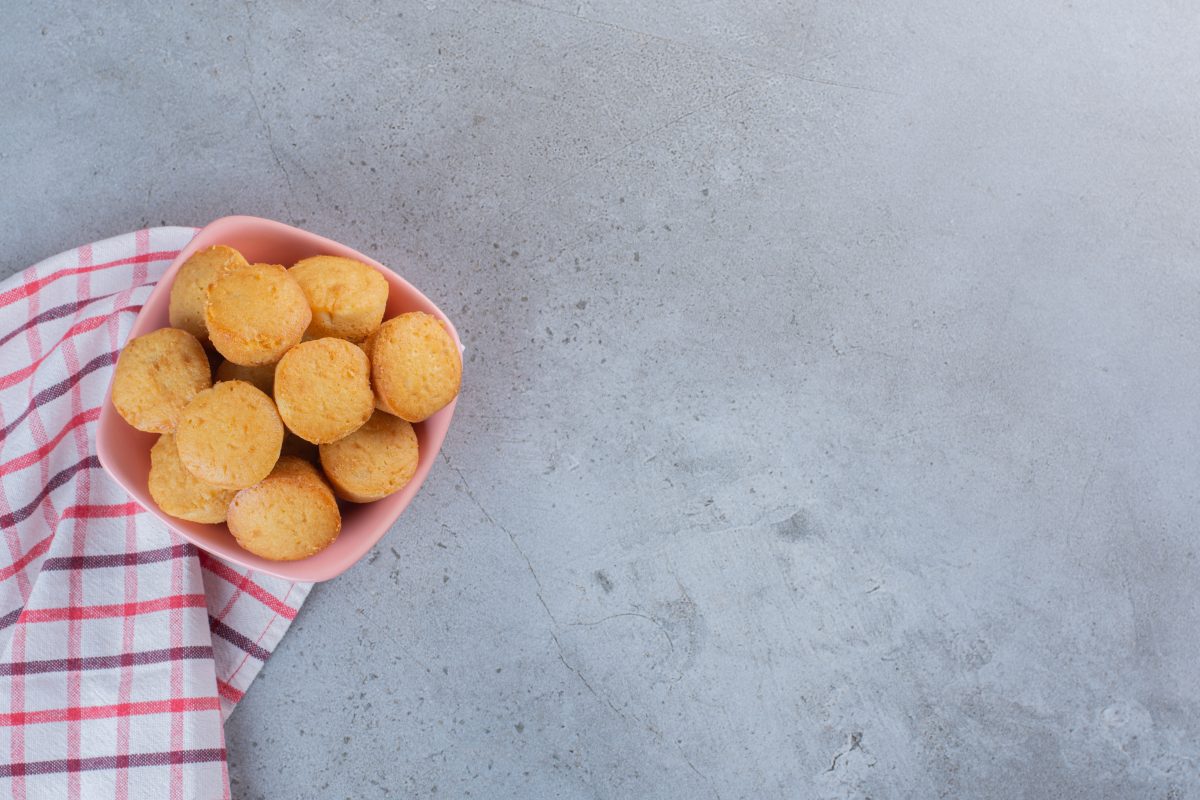 Pink bowl of mini sweet cakes on stone background