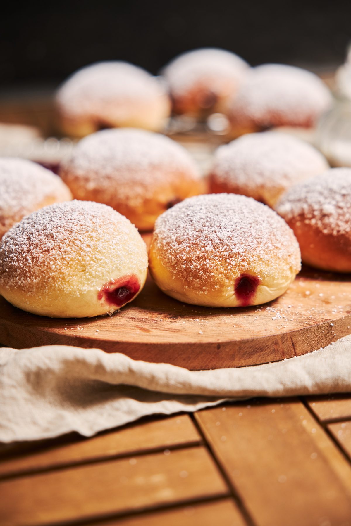 Vertical closeup of fluffy doughnuts filled with jam on a tray on the table under the lights