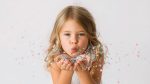 Little Girl Blowing Colorful Confetti Against a White Background