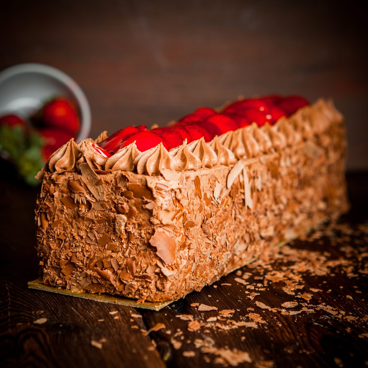 Side vew chocolate cream cake with chocolate chips and strawberry on wood background