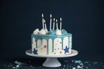 White birthday drip cake with teal ganache, star toppers and fun candles over dark blue background, generate ai