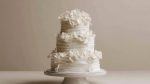 Elegant three tier wedding cake decorated with white floral accents on a simple stand