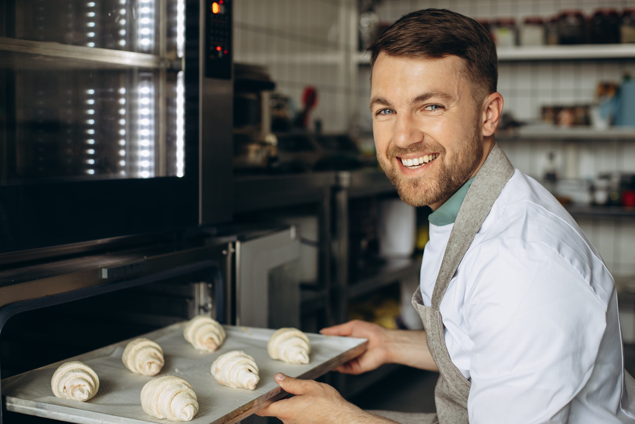 Man baker puts croissants dough into the oven